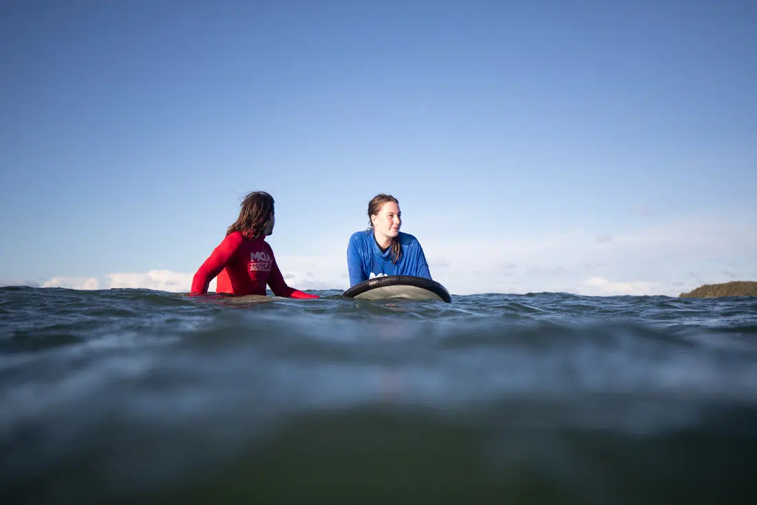 Surf instructor and student sitting on their boards in the water at Spot X
