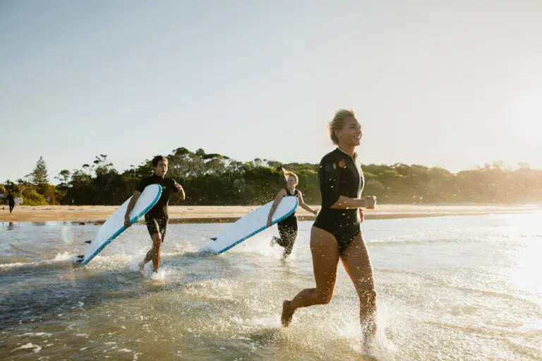 Surfer running into the sea with her board at sunrise