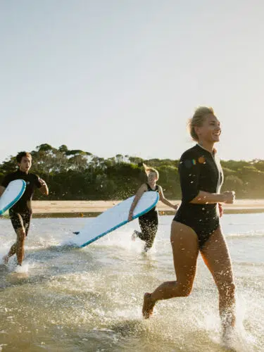 Surfer running into the sea with her board at sunrise