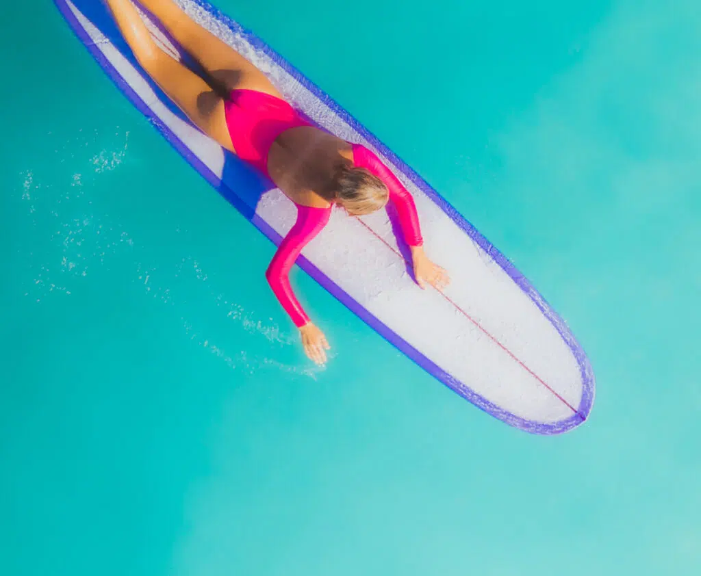 Surfer lying on a pink surfboard in clear blue water