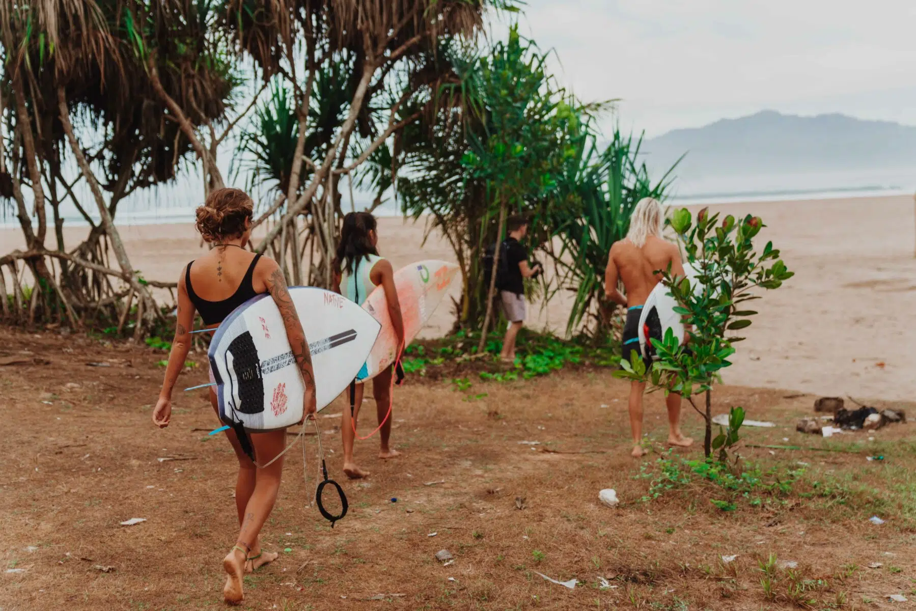 Surfers carrying boards along a tropical beach path