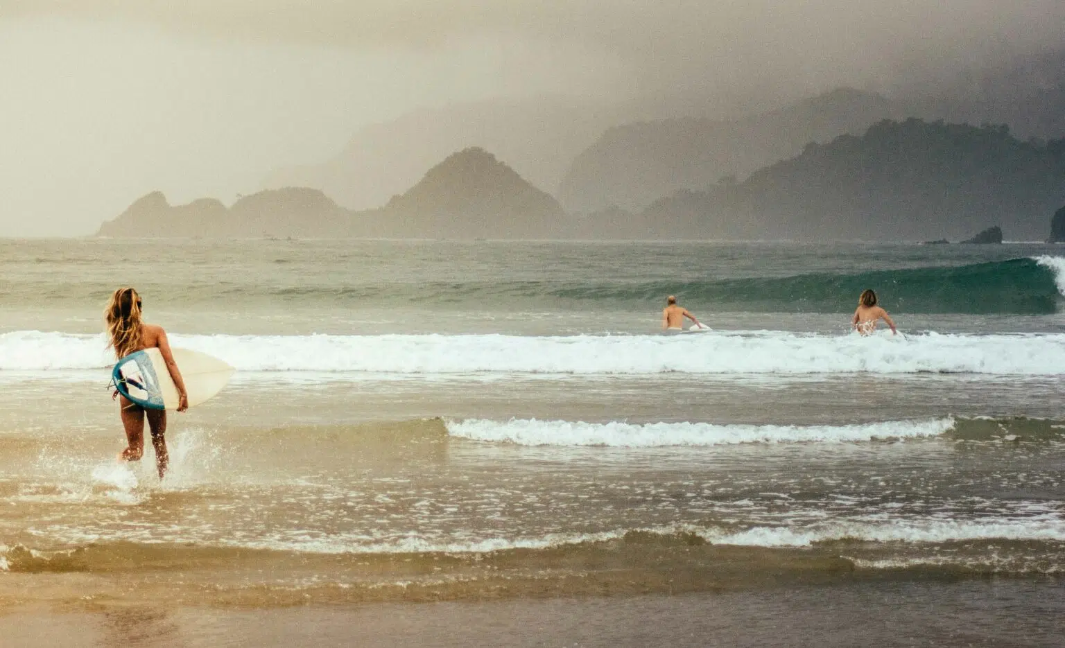 Surfer walking into the waves on a misty beach
