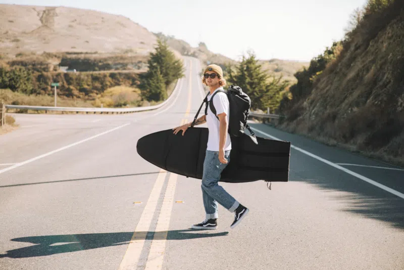 Traveller crossing a road carrying a surfboard bag