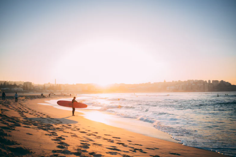 Surfer walking along the beach with a board at sunset