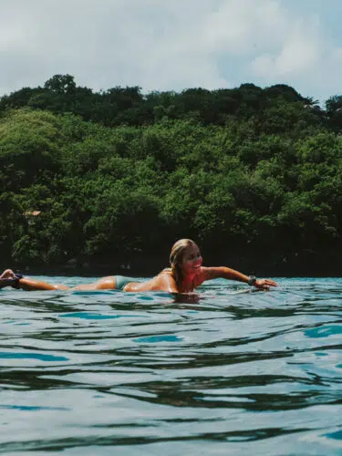 Surfer paddling near a green headland at Nusa Lembongan