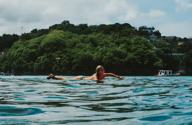 Surfer paddling near a green headland at Nusa Lembongan