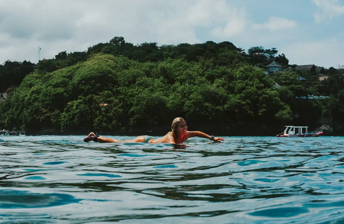 Surfer paddling near a green headland at Nusa Lembongan