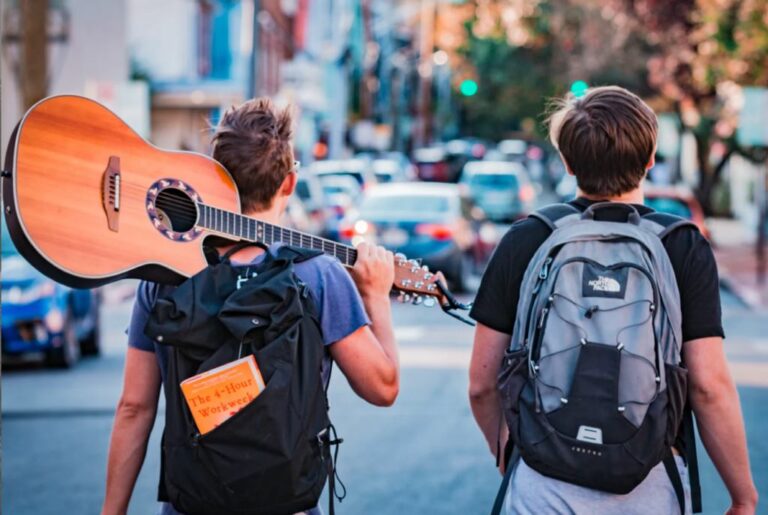Backpackers with a guitar walking down a city street