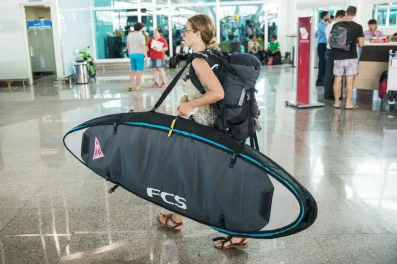 Traveller carrying a surfboard bag through an airport