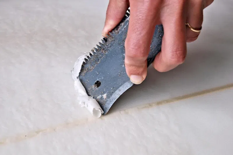 Scraping old wax off a surfboard
