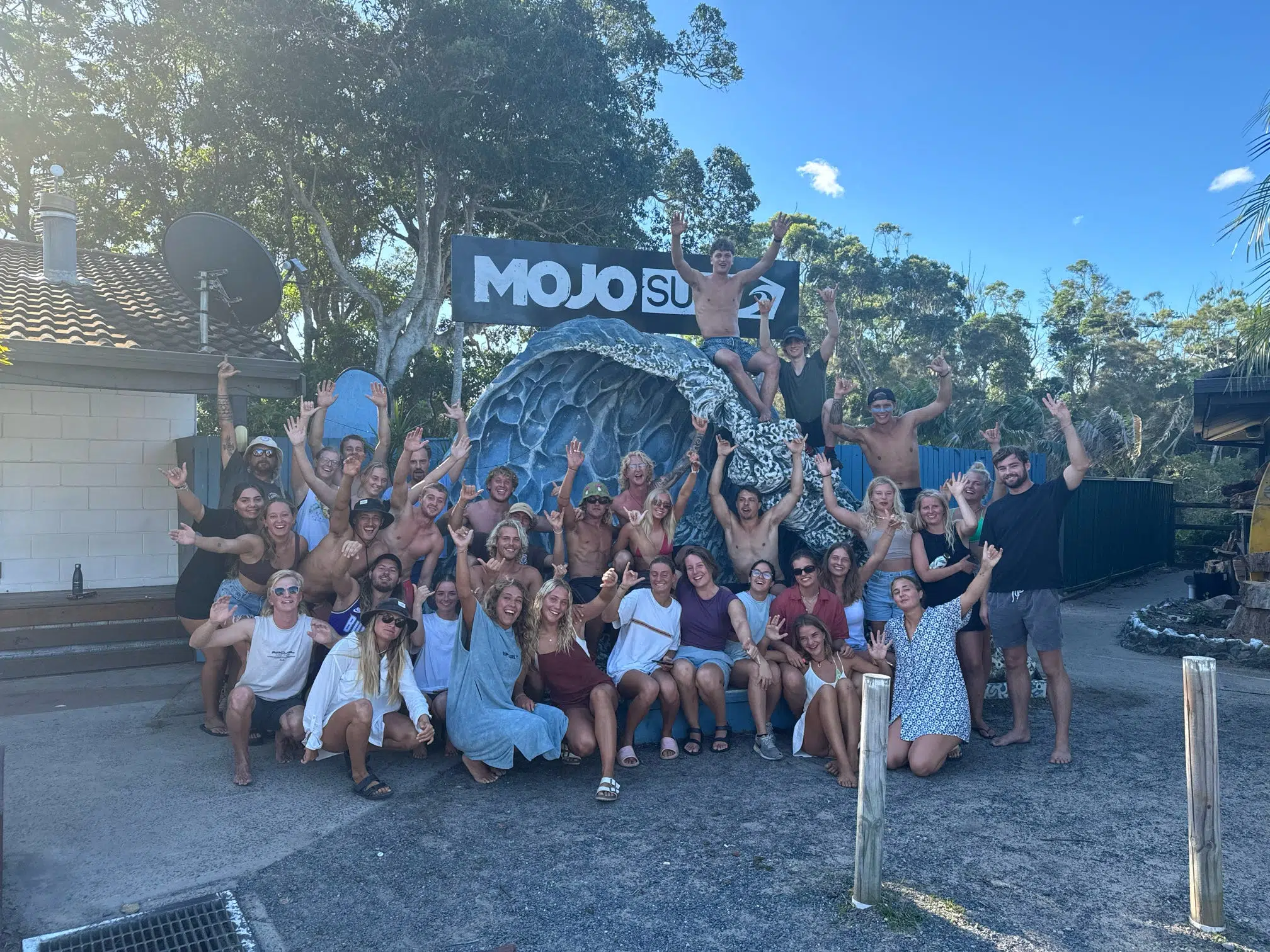 Big group of Mojosurf guests in front of the camp sign