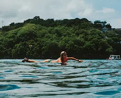 Surfer floating in the ocean near a green headland